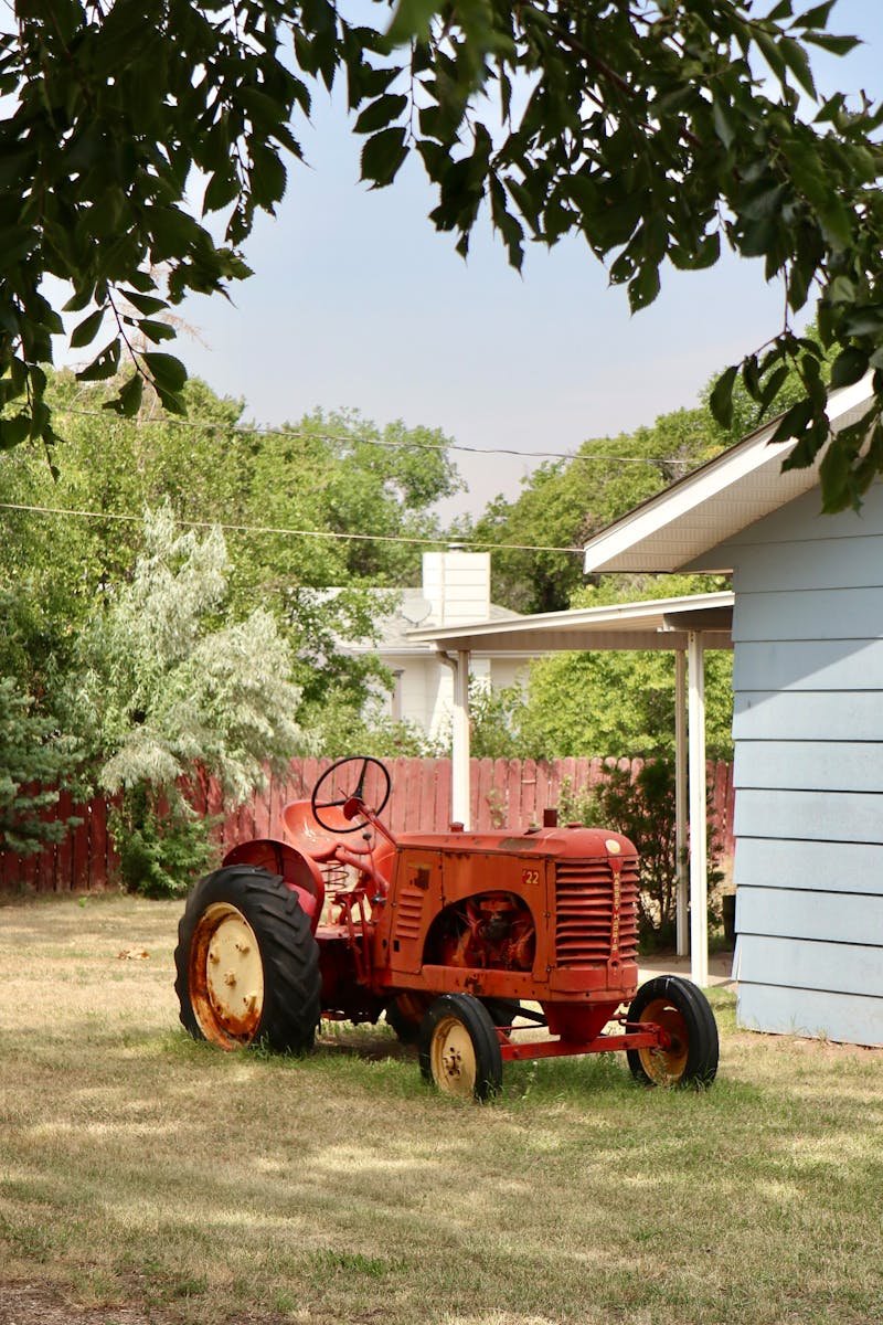 A charming red tractor parked near a barn under the sunlight in a rural area.